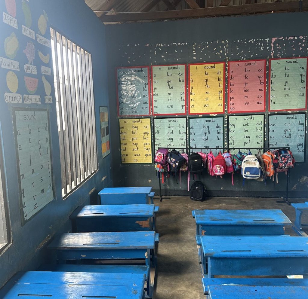 Luokkahuone, jossa siniseksi maalatut pulpetit, seinustalla kirjaintauluja ja lasten reppuja