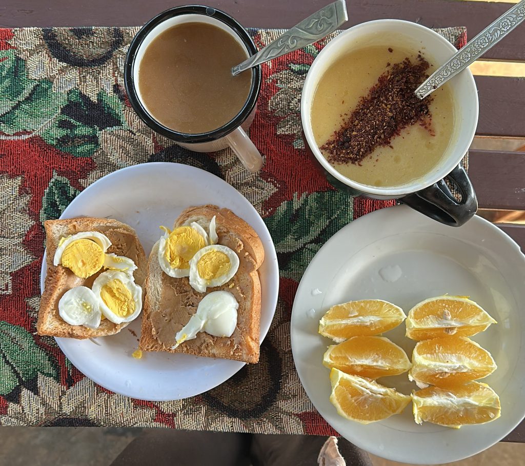 Pöydällä lautanen jolla kaksi palaa leipää, kahvikuppi, puurokuppi, toisella lautasella appelsiininlohkoja.