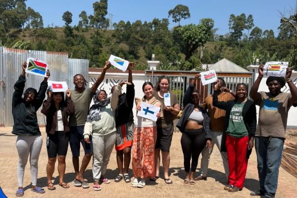 Ryhmä ihmisiä poseeraa kameralle pidellen käsissään eri maiden lippuja
