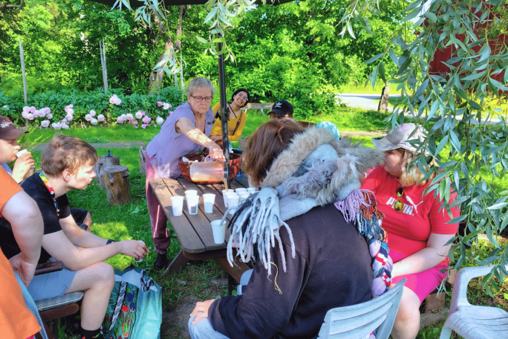 Ryhmä ihmisiä istuu pöydän ympärillä vehreässä ympäristössä