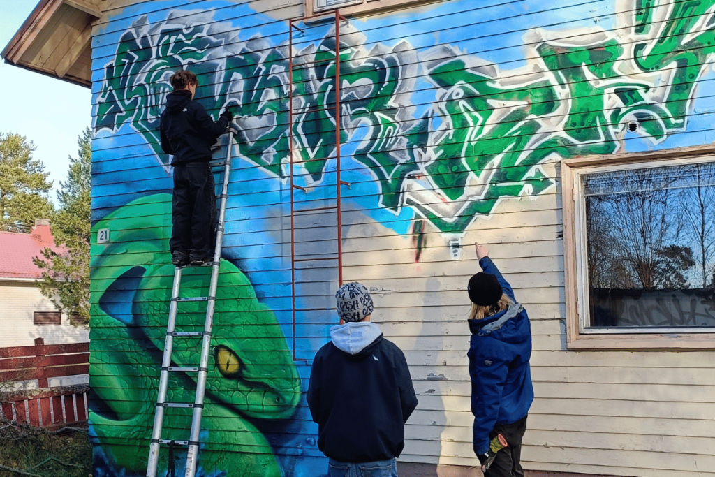 henkilö maalaa talon seinään graffitia
