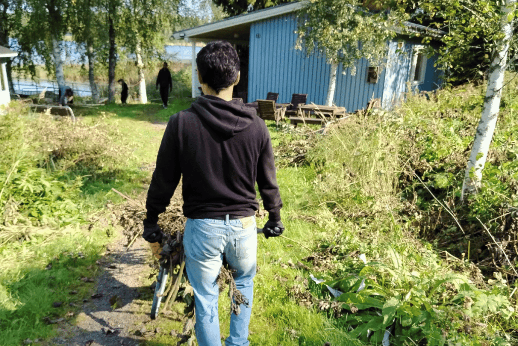 Takaa kuvattu henkilö siirtää oksia kottikärryssä luontomaisemassa